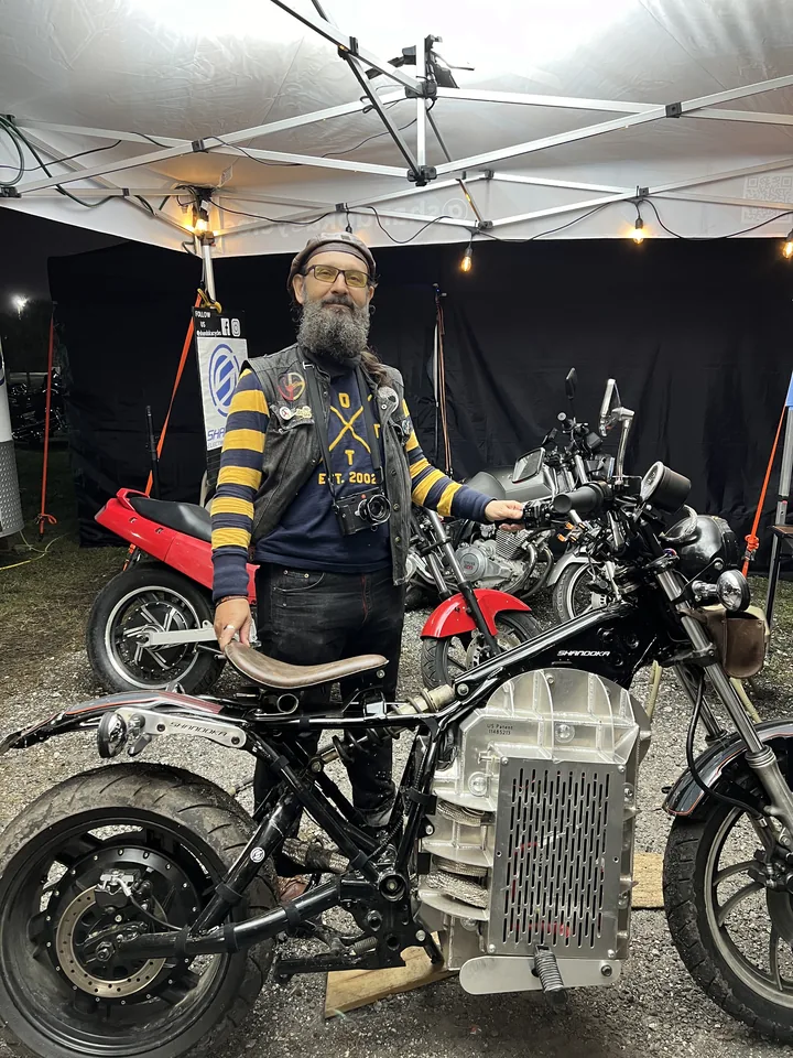 A technician standing with a converted bike under a work tent, the controller and pack exposed.