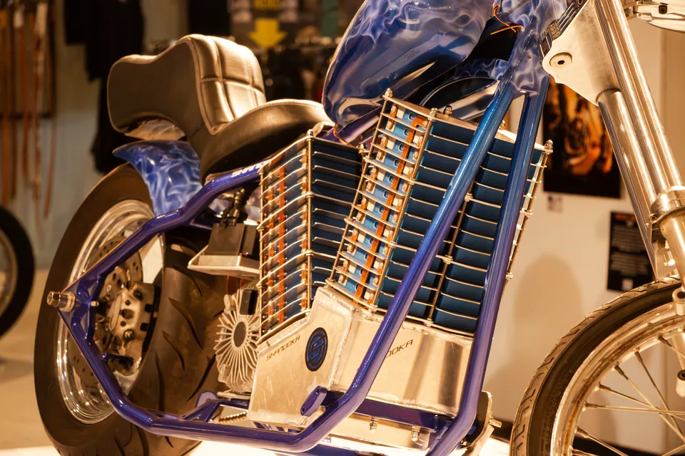 El frente del chopper y el soporte del motor de cerca, con los rieles azules del chasis a los lados del bloque de baterías.
